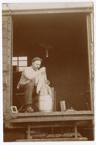 Un homme assis fait sa lessive sur le seuil du wagon.