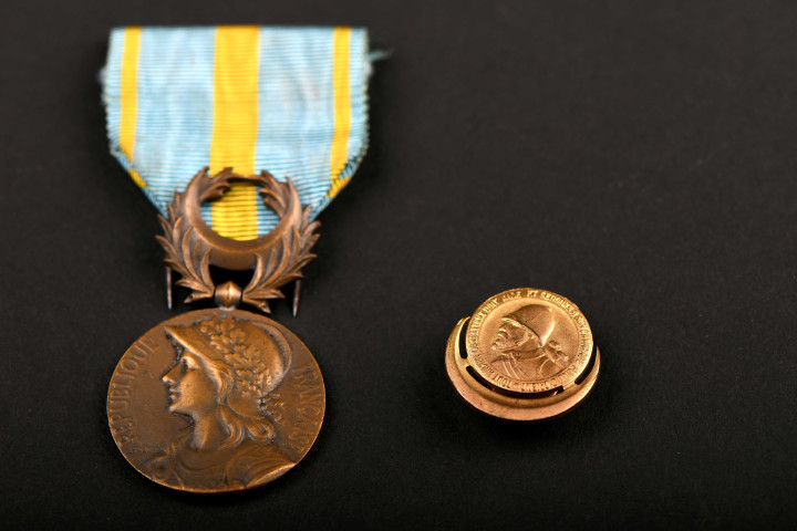Médaille commémorative d'Orient avec inscription « ORIENT » au dos, à l'avant l'inscription « REPUBLIQUE FRANCAISE », tenue par un ruban bleu d'une largeur de 36 mm coupé dans le sens de sa longueur de trois raies jaunes, celle du milieu ayant une largeur de cinq mm et celles des bords deux mm et une boutonnière avec inscription « TOUT ANCIEN COMBATTANT DOIT AIDE ET SECOURS A SON CAMARADE POILU D'ORIENT » : médailles commémoratives militaire.