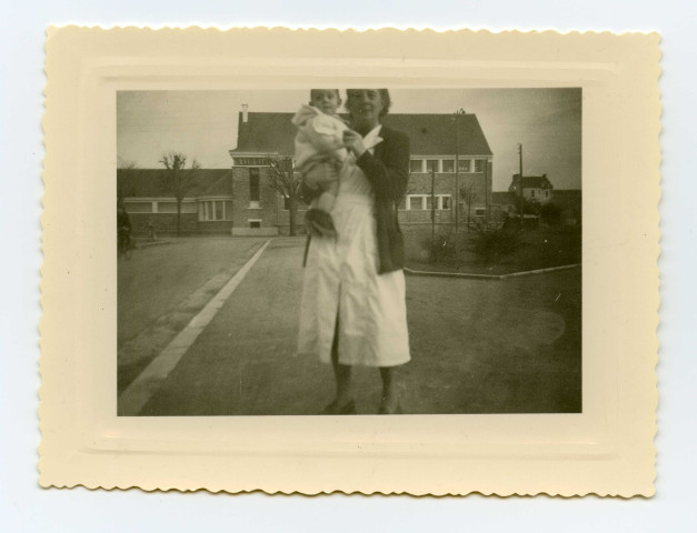 Simone Toussaint portant une jeune enfant devant l'Ecole Jean-Jaurès boulevard Victor-Hugo.
