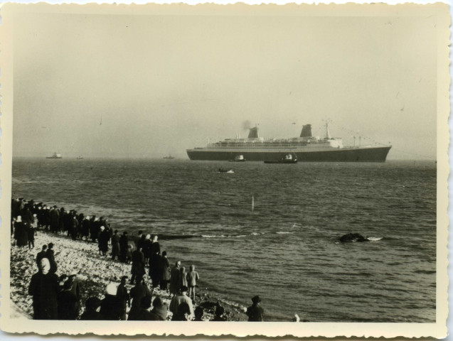Paquebot France en mer avec une foule de personnes au premier plan sur la plage.