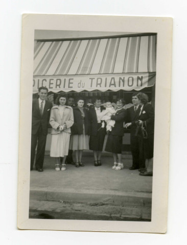Portrait de huit adultes et un nourisson devant le magasin tenu par la famille Toussaint