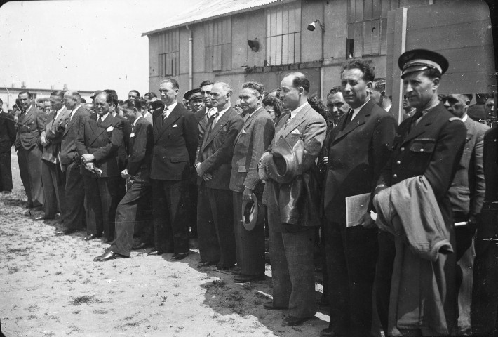 [Vue sur un groupe de personnalités civiles et militaires posant devant un bâtiment de type hangar] (1920-1950)