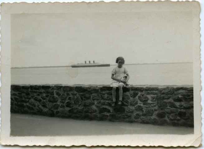 Une petite fille assise sur le perré boulevard Albert 1er. En arrière-plan, le paquebot Paris.